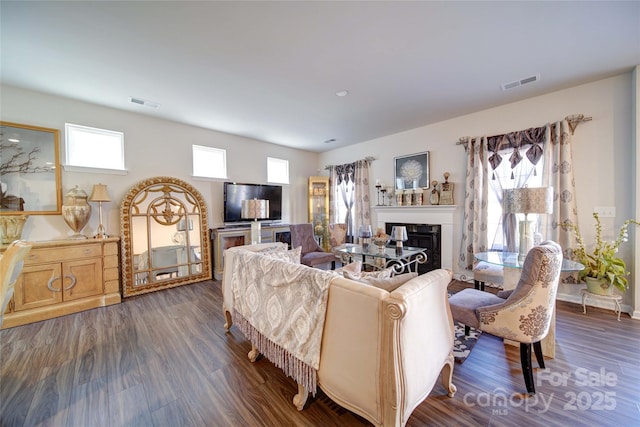 living room featuring a glass covered fireplace, dark wood-type flooring, and visible vents
