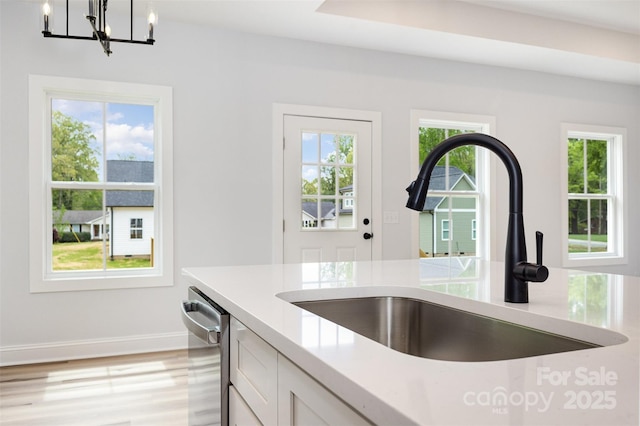 kitchen featuring baseboards, an inviting chandelier, stainless steel dishwasher, a sink, and hanging light fixtures