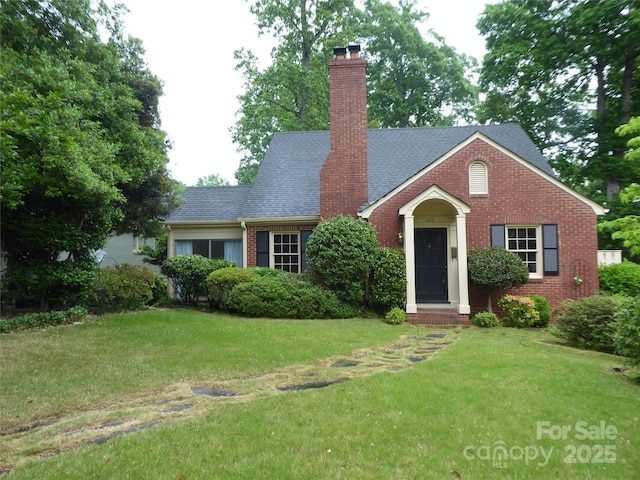 view of front facade featuring a chimney, a front yard, a shingled roof, and brick siding