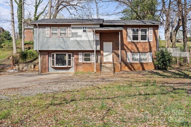 split foyer home with brick siding, entry steps, and a front lawn