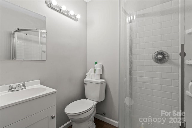 bathroom with a tile shower, toilet, vanity, and baseboards