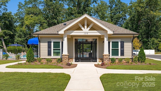 view of front facade with stone siding, roof with shingles, a front lawn, and fence