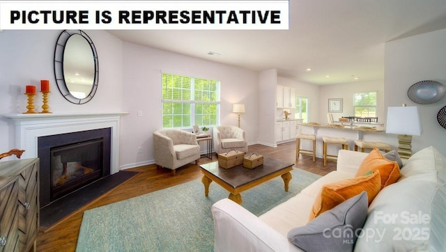 living area with a glass covered fireplace, baseboards, wood finished floors, and recessed lighting