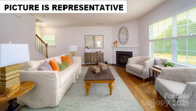 living area with a fireplace with flush hearth, wood finished floors, and stairs