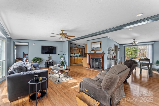 living room featuring a fireplace with raised hearth, a ceiling fan, light wood-type flooring, and a textured ceiling