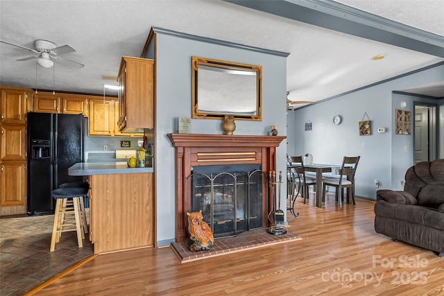 kitchen with black fridge with ice dispenser, light wood-style flooring, a fireplace, and a ceiling fan