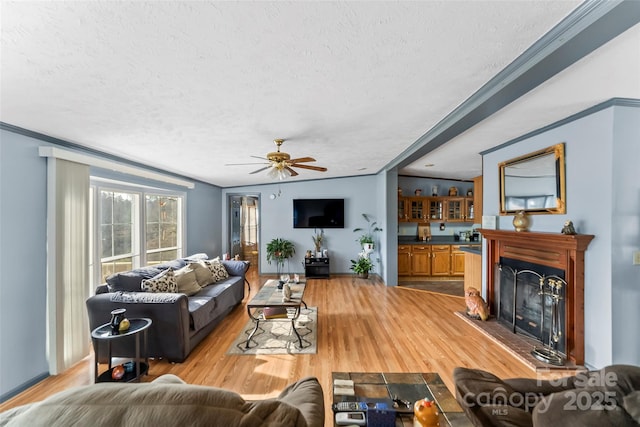 living room featuring light wood finished floors, a fireplace with raised hearth, a textured ceiling, and ceiling fan