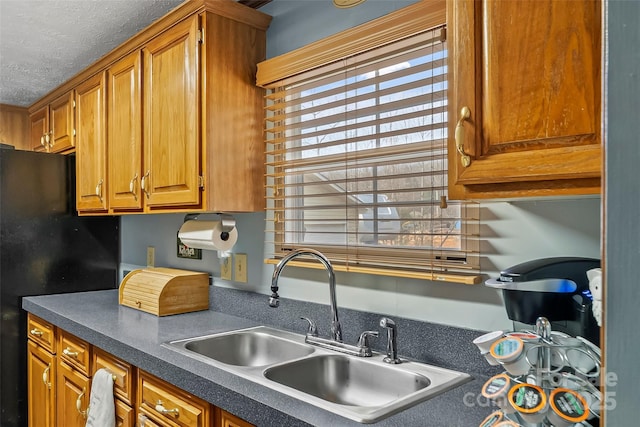 kitchen featuring brown cabinets, a sink, dark countertops, a textured ceiling, and freestanding refrigerator