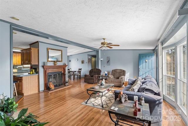 living room featuring a textured ceiling, a fireplace with raised hearth, light wood-type flooring, and ceiling fan