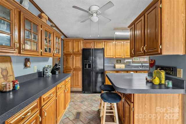 kitchen with dark countertops, glass insert cabinets, ceiling fan, black fridge with ice dispenser, and a textured ceiling