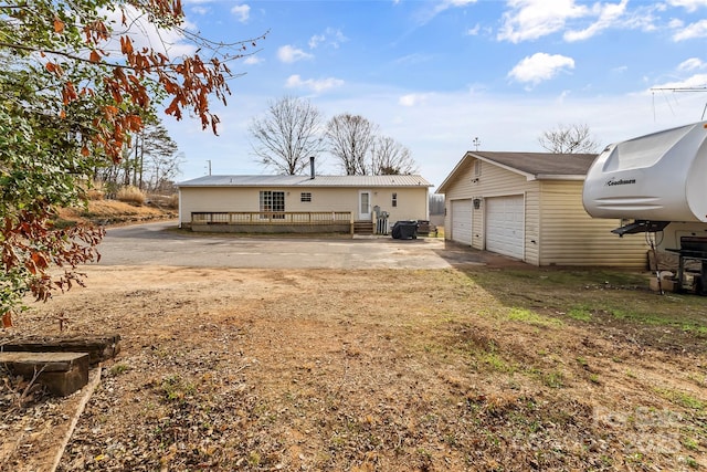 back of property featuring a deck, driveway, a detached garage, and an outdoor structure