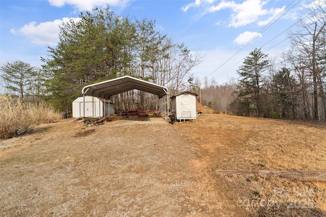 view of yard featuring a carport, driveway, a storage unit, and an outbuilding