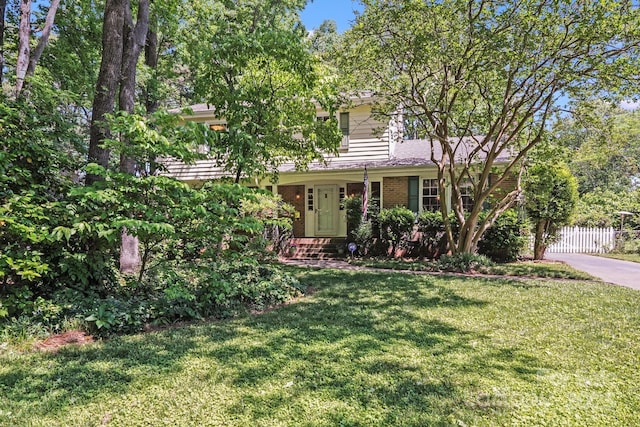 view of property hidden behind natural elements featuring brick siding, fence, and a front yard