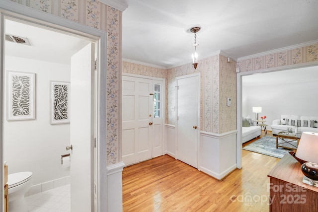 entrance foyer featuring light wood-style flooring, baseboards, wallpapered walls, visible vents, and ornamental molding
