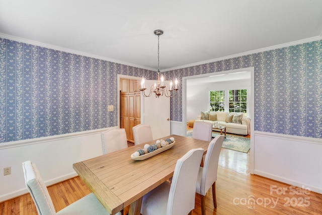 dining room featuring crown molding, wallpapered walls, wood finished floors, and a chandelier