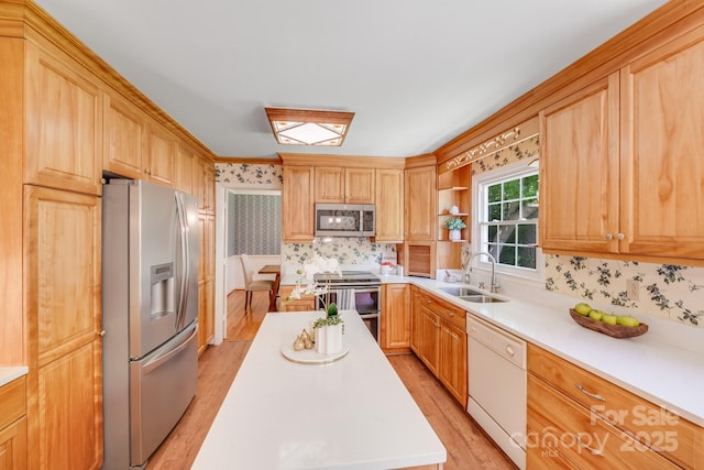 kitchen with wallpapered walls, light countertops, a sink, light wood-style flooring, and appliances with stainless steel finishes
