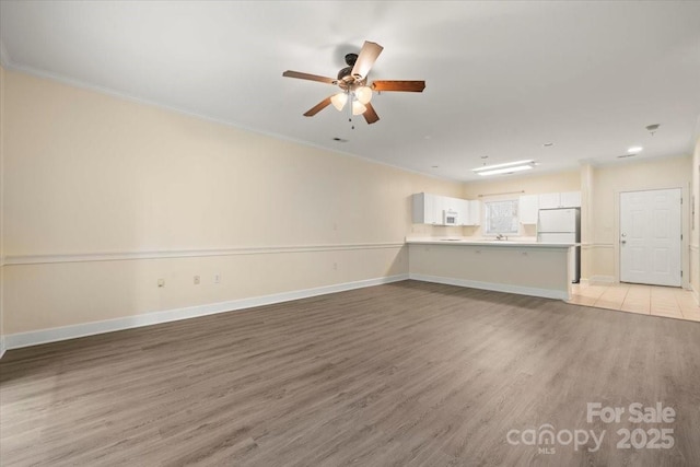 unfurnished living room featuring light wood finished floors, ornamental molding, baseboards, and a ceiling fan