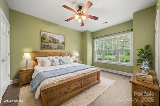 bedroom with a ceiling fan, visible vents, wood finished floors, and baseboards