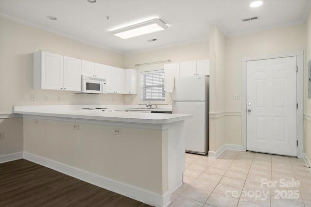 kitchen with white appliances, visible vents, white cabinetry, a peninsula, and light countertops