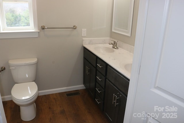 bathroom featuring wood finished floors, baseboards, double vanity, a sink, and toilet