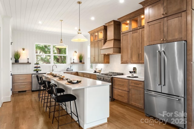 kitchen with premium range hood, high quality appliances, wood finished floors, and light countertops