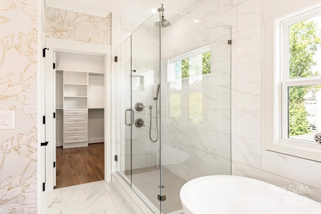 full bath featuring a freestanding tub, marble finish floor, a walk in closet, and a shower stall
