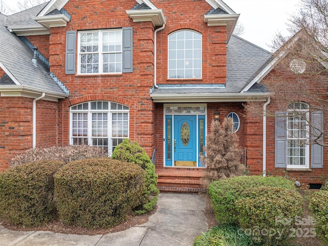 view of exterior entry with brick siding and roof with shingles