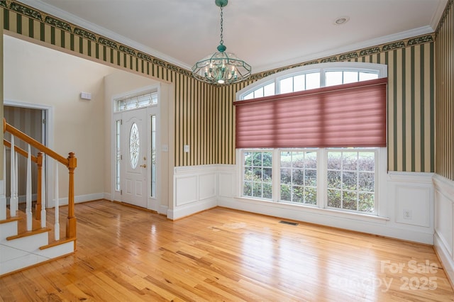 foyer with wallpapered walls, a chandelier, stairs, wainscoting, and wood finished floors