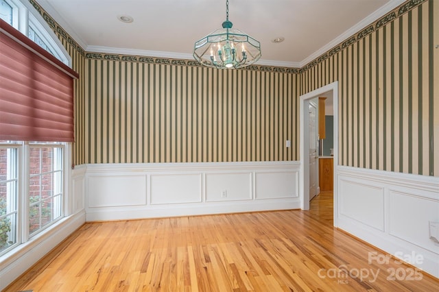 spare room with a notable chandelier, wallpapered walls, crown molding, and light wood-style floors