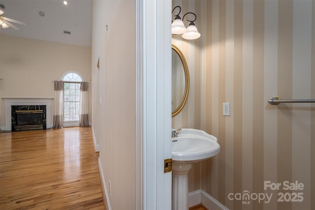 bathroom featuring wood finished floors, a high end fireplace, wallpapered walls, baseboards, and ceiling fan