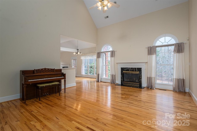 unfurnished living room with light wood finished floors, ceiling fan with notable chandelier, high vaulted ceiling, and a premium fireplace