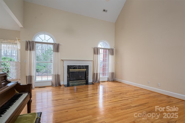 living room featuring visible vents, baseboards, a premium fireplace, wood finished floors, and high vaulted ceiling