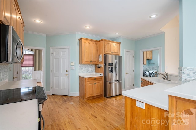 kitchen with light wood finished floors, a sink, decorative backsplash, light countertops, and stainless steel appliances