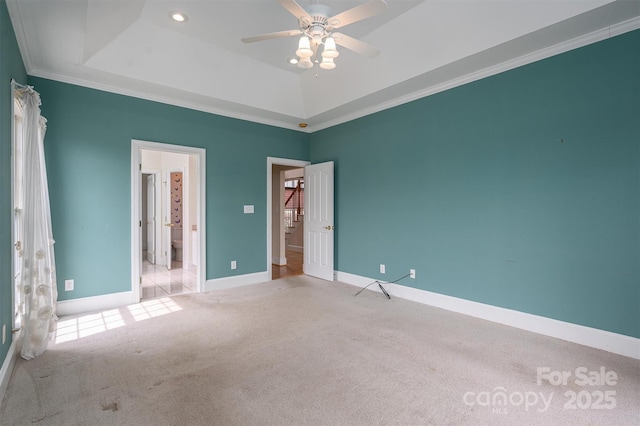 unfurnished bedroom featuring baseboards, a tray ceiling, ceiling fan, crown molding, and carpet flooring