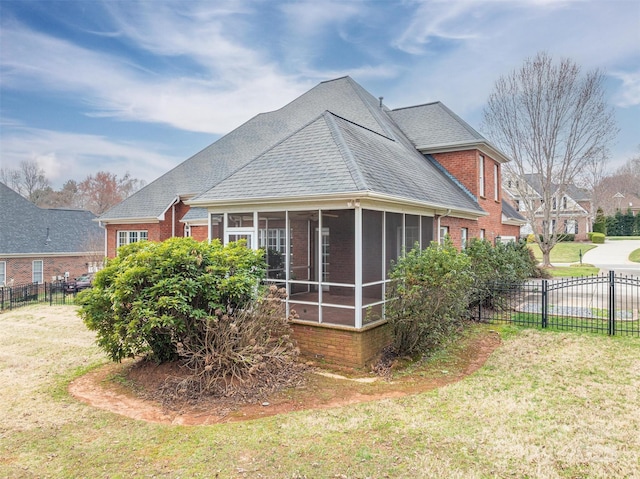 view of side of property with fence, a yard, roof with shingles, a sunroom, and brick siding