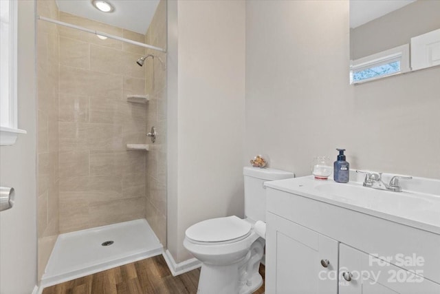 full bath with baseboards, toilet, a tile shower, wood finished floors, and vanity