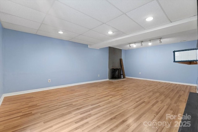 finished basement featuring a paneled ceiling, baseboards, and wood finished floors