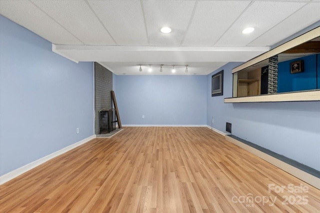 finished basement with a brick fireplace, baseboards, and wood finished floors