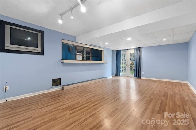 unfurnished living room with track lighting, wood finished floors, baseboards, and a drop ceiling