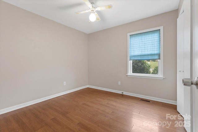 empty room with ceiling fan, visible vents, baseboards, and wood finished floors