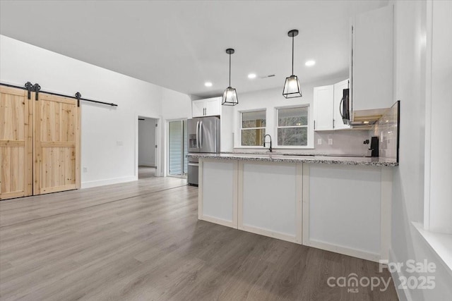 kitchen featuring light stone counters, stainless steel fridge, white cabinets, and light wood-type flooring