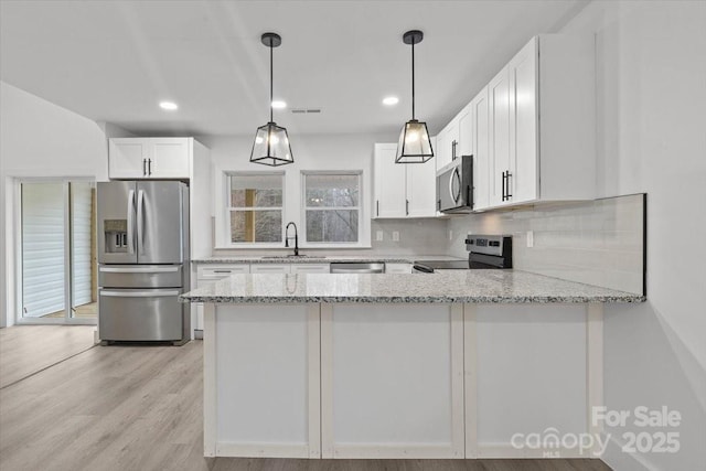 kitchen with light stone countertops, a peninsula, a sink, decorative backsplash, and appliances with stainless steel finishes