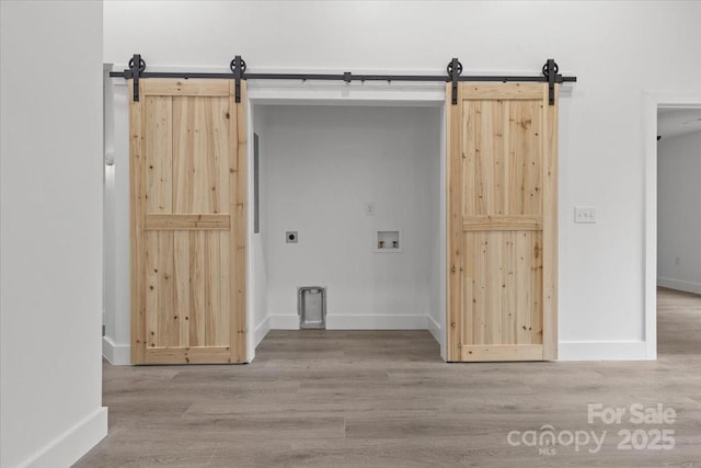 clothes washing area featuring laundry area, wood finished floors, a barn door, and washer hookup