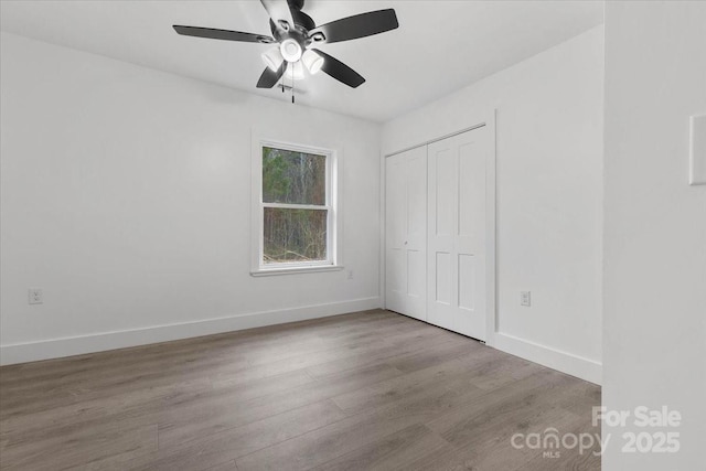 unfurnished bedroom with a closet, baseboards, wood finished floors, and a ceiling fan