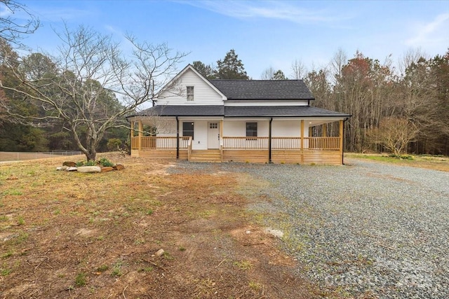 farmhouse inspired home featuring gravel driveway, a porch, and a shingled roof