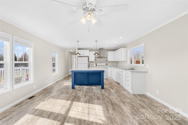 kitchen featuring visible vents, a center island, light wood-style floors, white appliances, and wall chimney exhaust hood