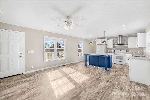 kitchen with a center island, wall chimney range hood, white appliances, a ceiling fan, and a sink