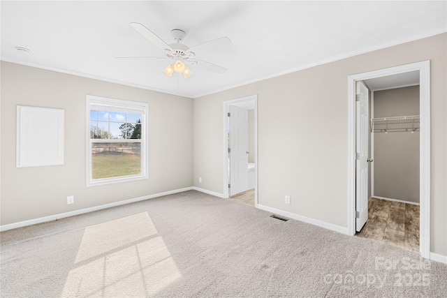 unfurnished bedroom with a spacious closet, visible vents, crown molding, and carpet