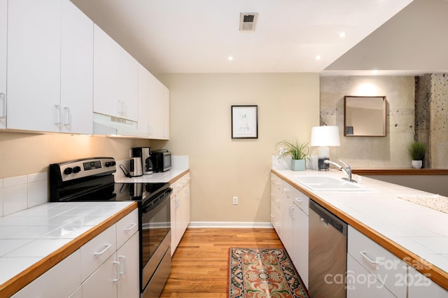 32 Broadway St Unit 330, Asheville, NC 28801 - kitchen featuring stainless steel appliances, tile counters, light wood-type flooring, white cabinetry, and a sink