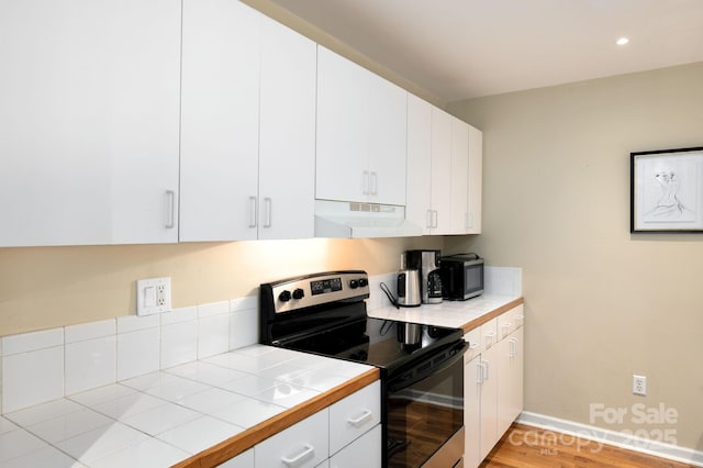 32 Broadway St Unit 330, Asheville, NC 28801 - kitchen featuring stainless steel appliances, under cabinet range hood, tile countertops, light wood-type flooring, and white cabinetry